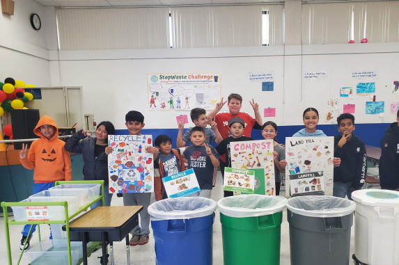 Students with signs standing in front of waste bin system in school cafeteria