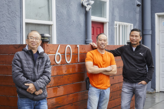 Three men posing in front of multifamily building. 