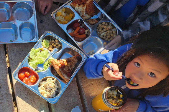 Reusable lunch trays on a wooden table with student looking up at the camera while eating.