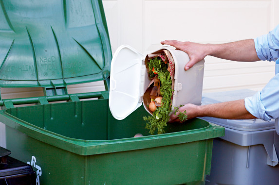 Person dumping foodscraps in kitchen pail into curbside green bin