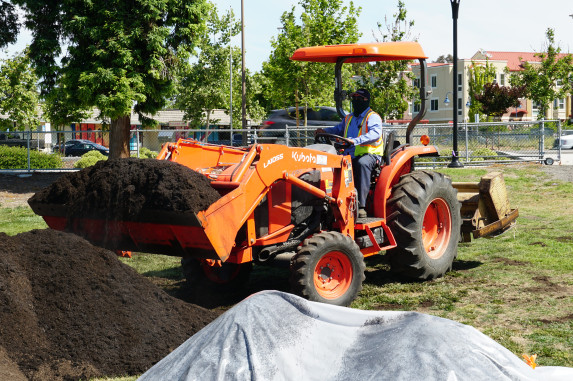 Orange tractor moving piles of compost