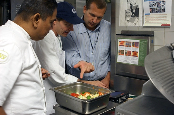 Three men looking at tray of food on scale