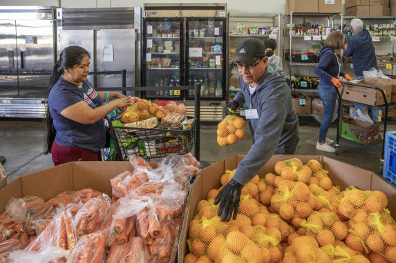 Man sorting surplus bags of fruit next to woman with shopping cart full of food