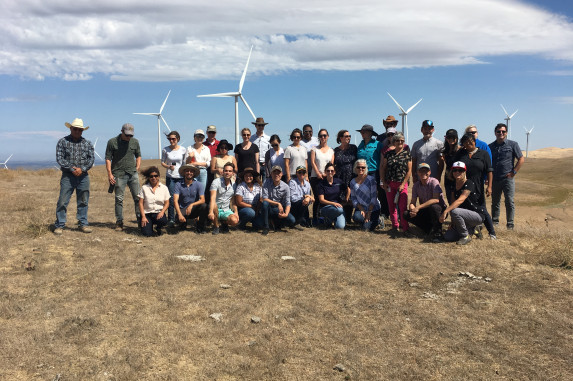 Group of people posing for photo in open field in front of wind mills