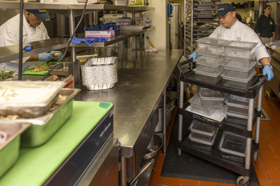Kitchen staff rolling a cart of reusable plastic food trays for storage