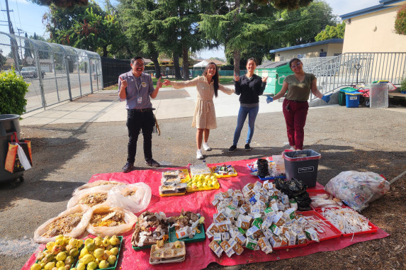 Four adults standing behind tarp with sorted waste items from school cafeteria