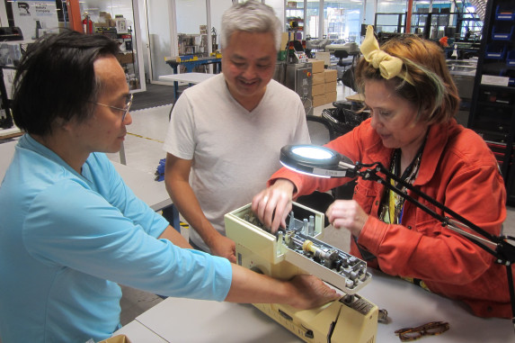 Three adults repairing sewing machine