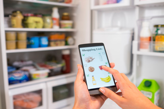 Person making a shopping list on their phone while browsing their refrigerator